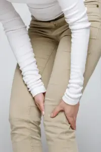 Arthritis-Treatment A woman wearing a white long-sleeve shirt and tan pants, clutching her knee, suffering from arthritis. Get arthritis treatment from Dr. David Lans in New Rochelle.