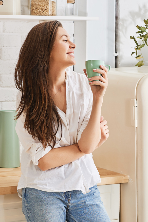 Food-Allergies-Treatment A woman in a white blouse holding a mint green mug in her kitchen smiles due to relief from food allergies. Get treatment for food allergies from Dr. David Lans in New Rochelle.