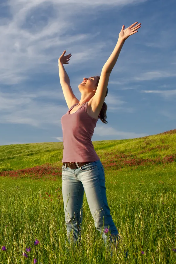 Graves-Disease-Treatment A woman in a tank top and jeans looks up with her arms outstretched to the sky in a field after successful treatment for Grave's Disease from Dr. David Lans in New Rochelle.