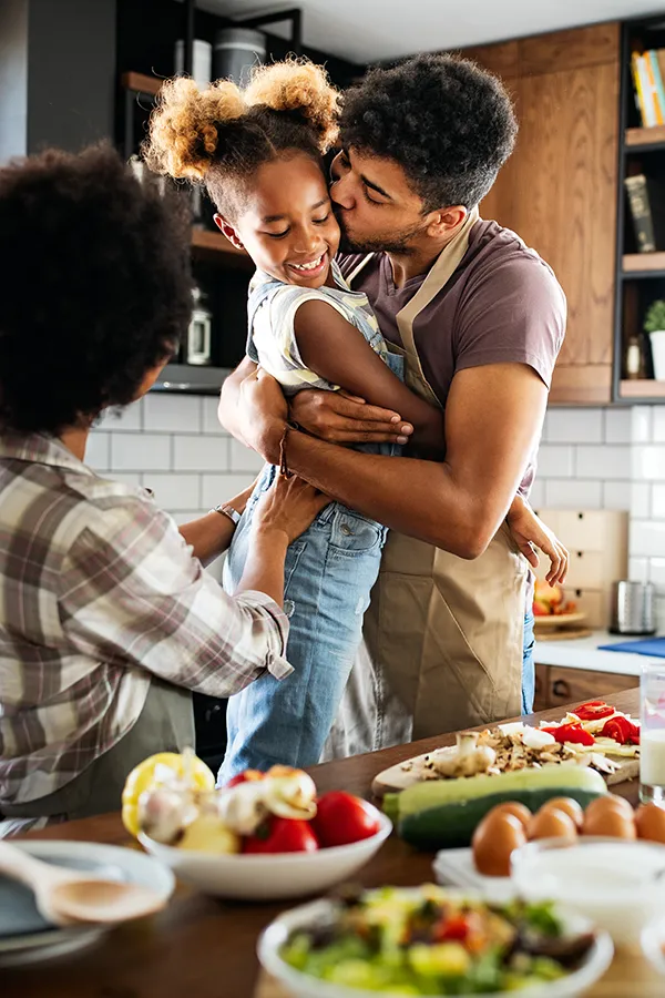 Gut-Health-Treatment A man holds his daughter and kisses her cheek as the family makes a healthy dinner in the kitchen. Get help for digestive issues and gut health from Dr. David Lans in New Rochelle.