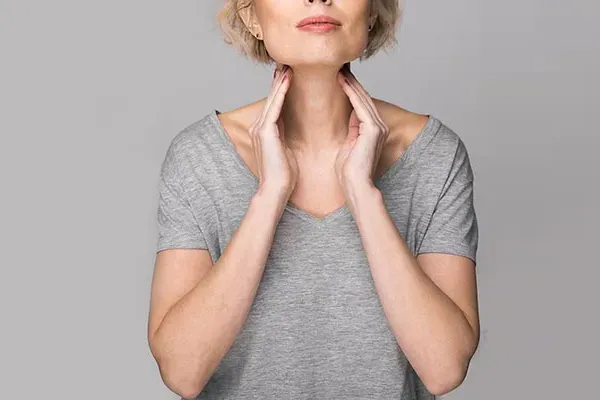 Hashimotos-Thyroiditis-Doctor An older blonde woman in a gray t-shirt holds her hands to her neck checking for signs of thyroid problems. Get help for Hashimoto's Thyroiditis from Dr. David Lans in New Rochelle.