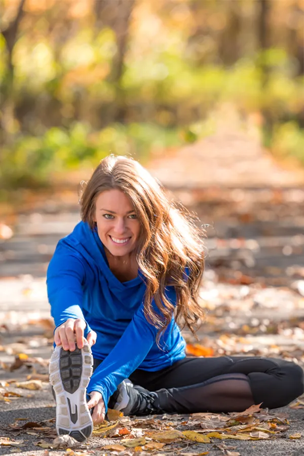 PRP-for-Sports-and-Orthopedics-Treatment A woman in blue warm ups stretching and preparing for a run on an outdoor trail. Get Platelet Rich Plasma (PRP) treatment for sports and orthopedics from Dr. David Lans in New Rochelle.