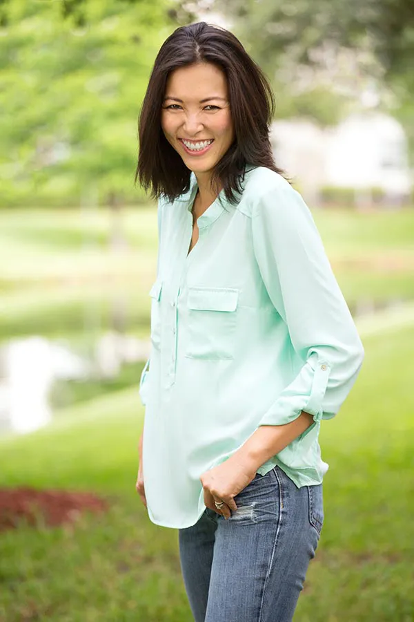 Perimenopause-Treatment A middle-aged brunette woman in a light green button-up shirt stands outside smiling, happy with her perimenopause treatment from Dr. David Lans in New Rochelle.